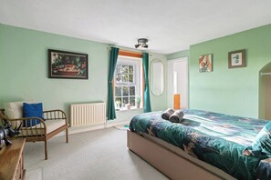 A room with a bed, a chair, a window with curtains, a radiator, and a ceiling fan. - Spacious 6-Bed Home Surrounded by Nature (Lincolnshire)