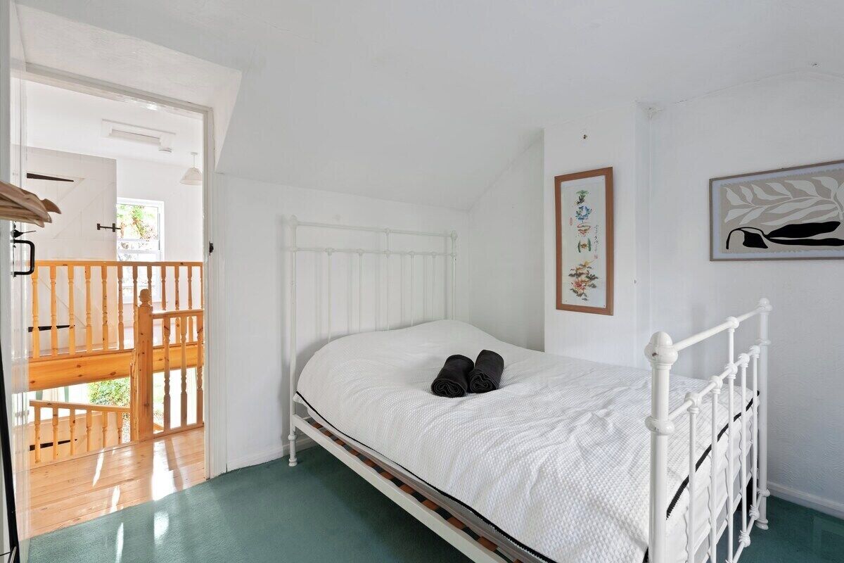 A white bed with a wooden headboard, a wooden door with a glass panel, and a framed picture on the wall.