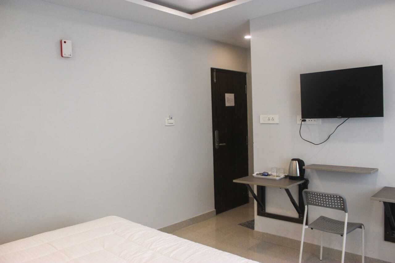 Une chambre d’hôtel avec un lit, un bureau et une chaise, un téléviseur fixé au mur et une porte.