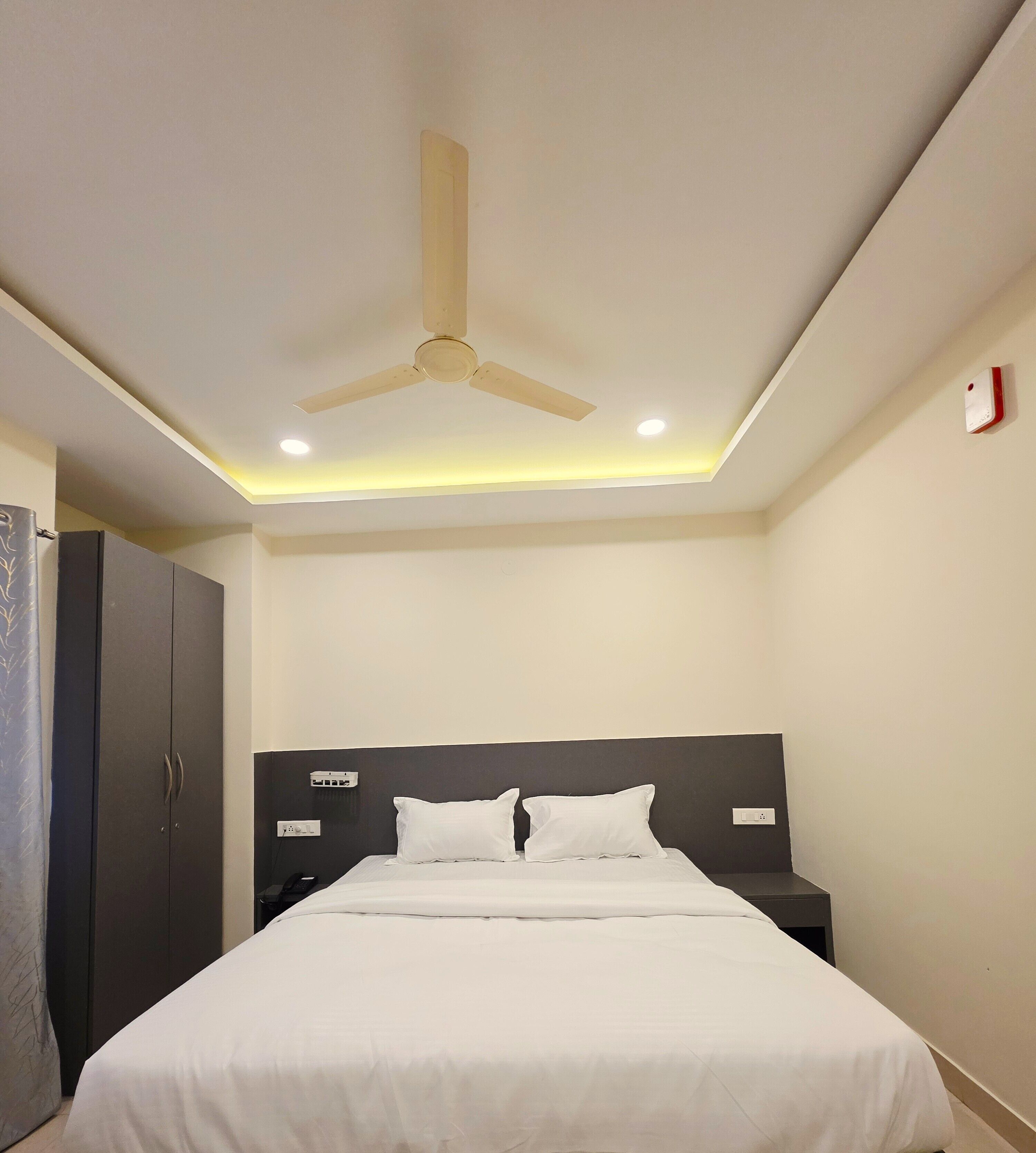 A neatly arranged bedroom with a bed, a wardrobe, a bedside table, and a ceiling fan.