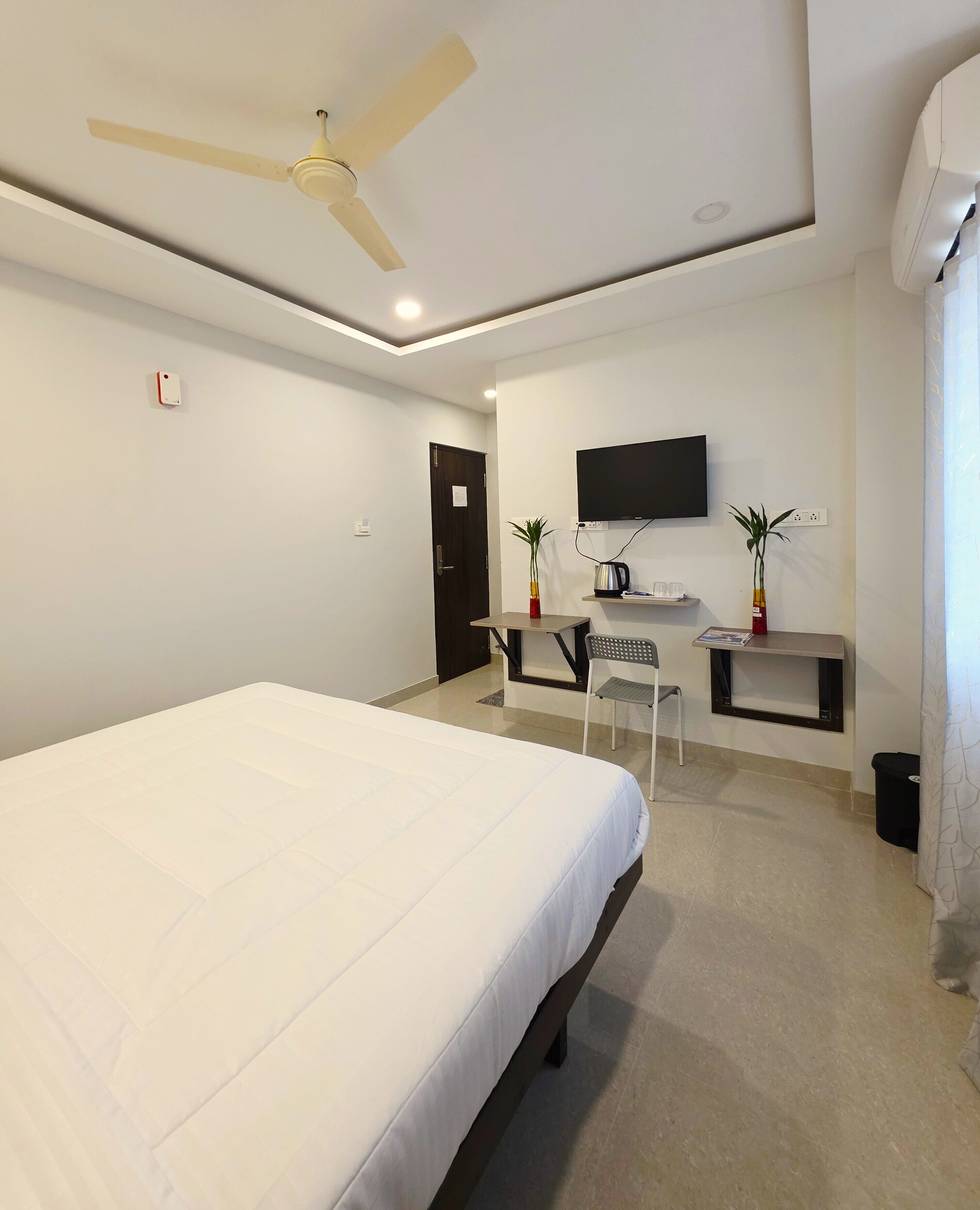 A hotel room with a bed, a desk with a chair, a television, and a ceiling fan.