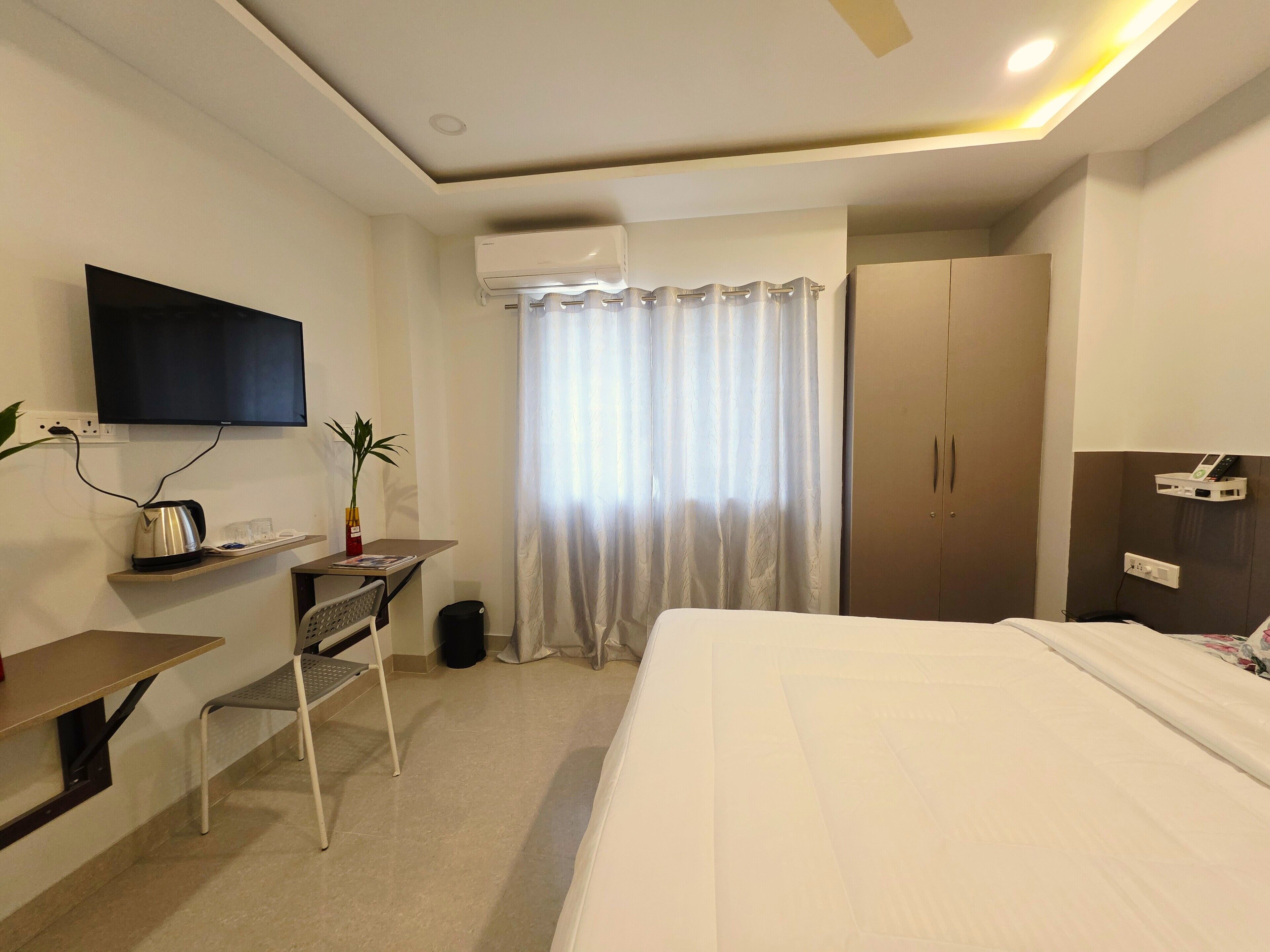 Ein Hotelzimmer mit einem Bett, einem Schreibtisch mit Stuhl, einem Fernseher, einem Kleiderschrank und einem Fenster mit Vorhängen.