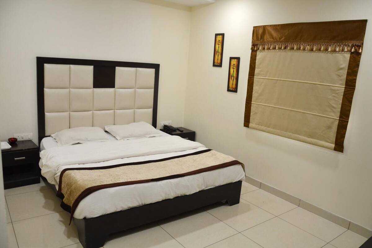 A bedroom with a large bed, a nightstand, a bedside table, and a window with curtains.