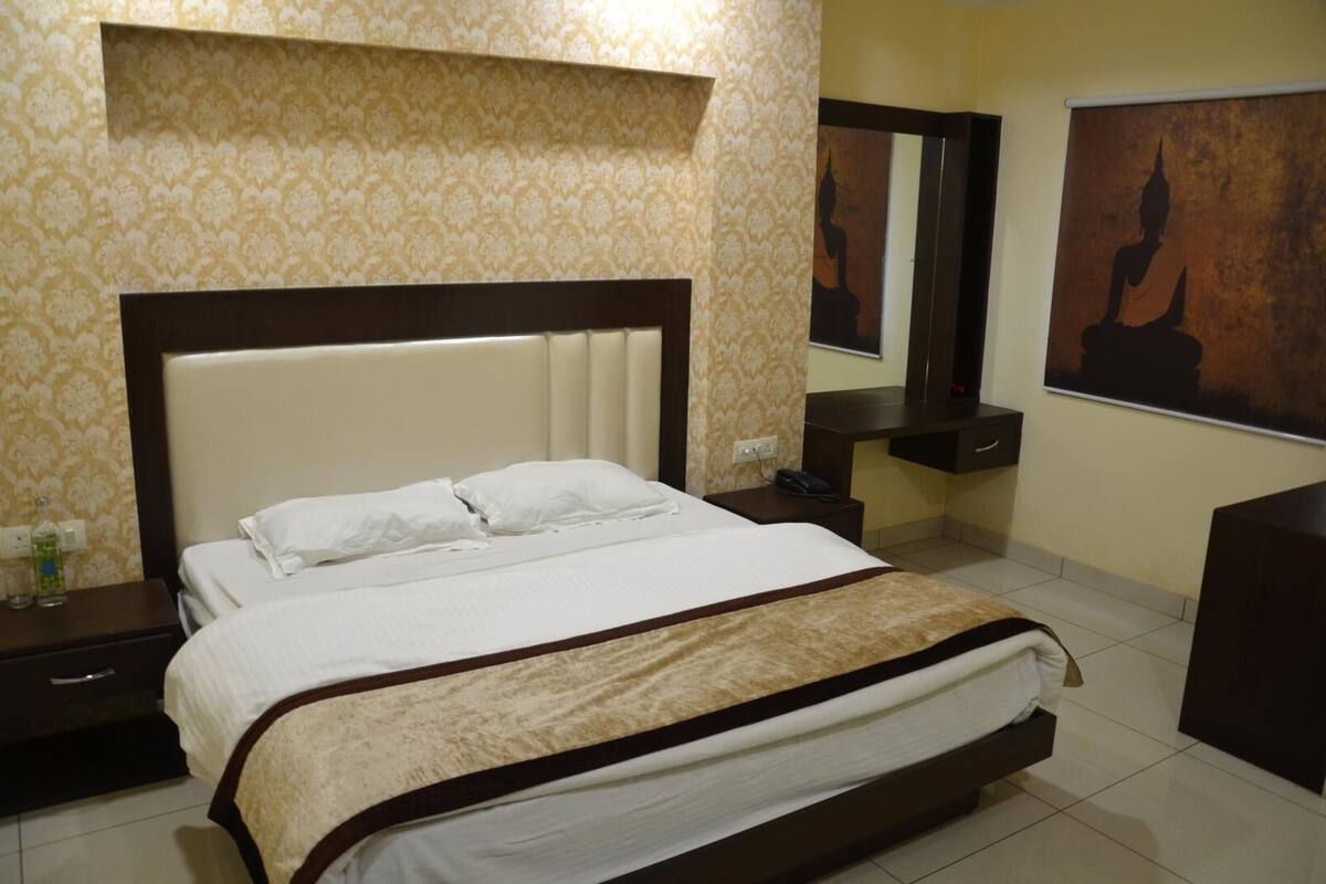 A hotel room with a large bed, a nightstand, a dresser, a mirror, and a wall with a Buddha painting.