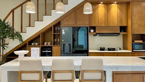 A modern kitchen with wooden cabinets, a built-in oven, a microwave, and a water dispenser. There is a staircase with wooden railings leading to an upper level.