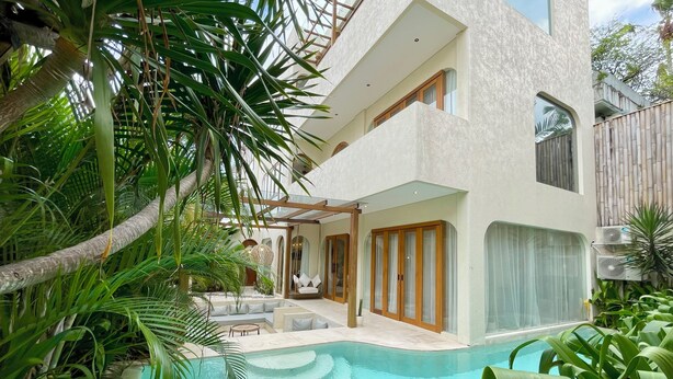 A modern house with a swimming pool, surrounded by lush greenery and a wooden fence.