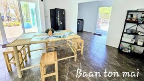 A spacious room with a large table, chairs, a refrigerator, and a shelving unit.