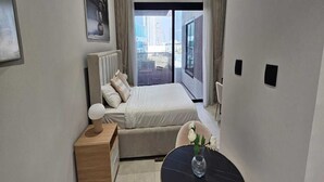 A modern bedroom with a bed, bedside table, and a view of the city through a large window.