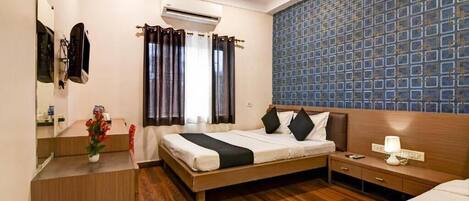 A hotel room with a bed, bedside table, nightstand, and a wall-mounted air conditioning unit.