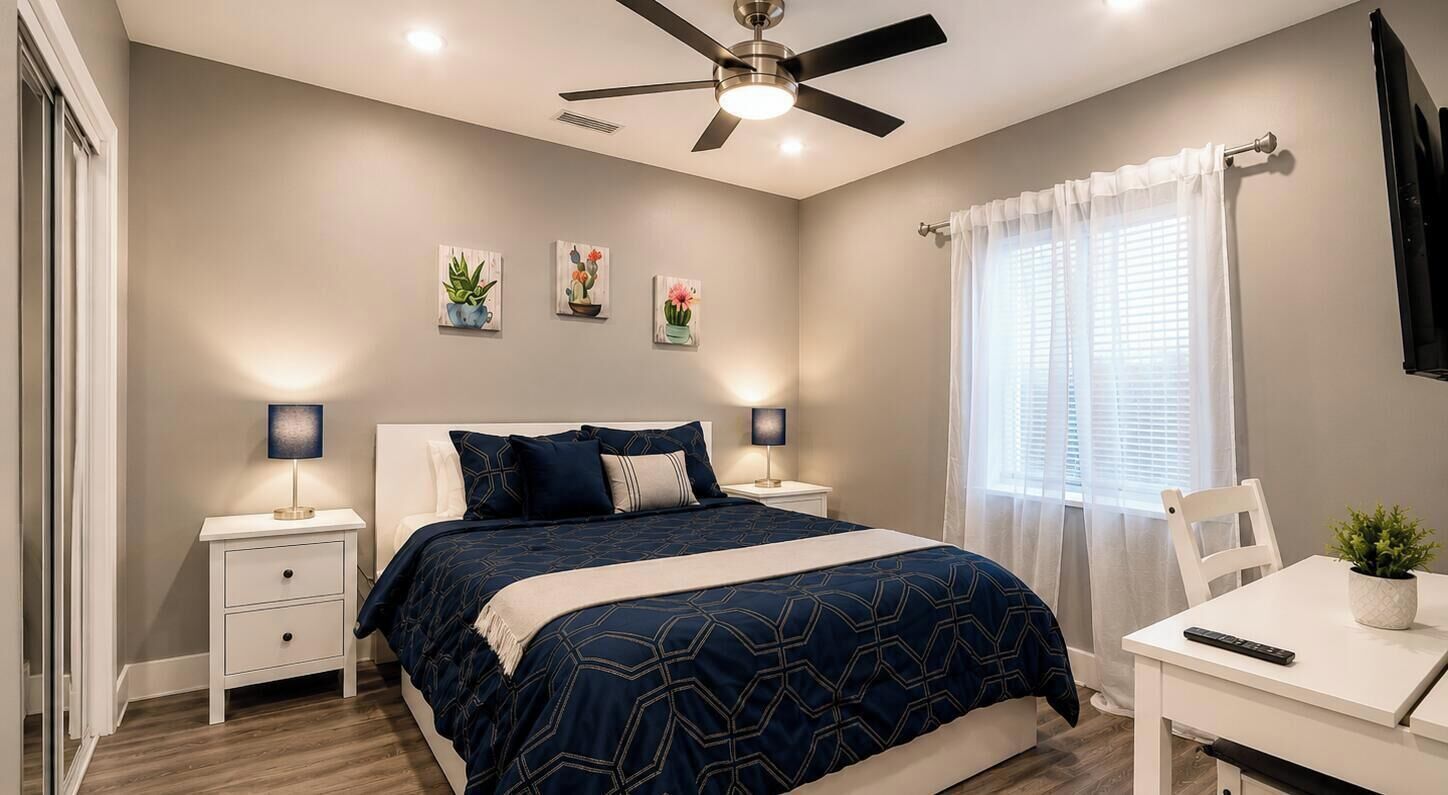 A bedroom with a bed, bedside tables, a desk, a ceiling fan, and a window with curtains.