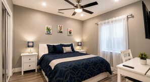 Une chambre à coucher comprenant un lit, des tables de chevet, un bureau, un ventilateur de plafond et des œuvres d’art accrochées au mur.