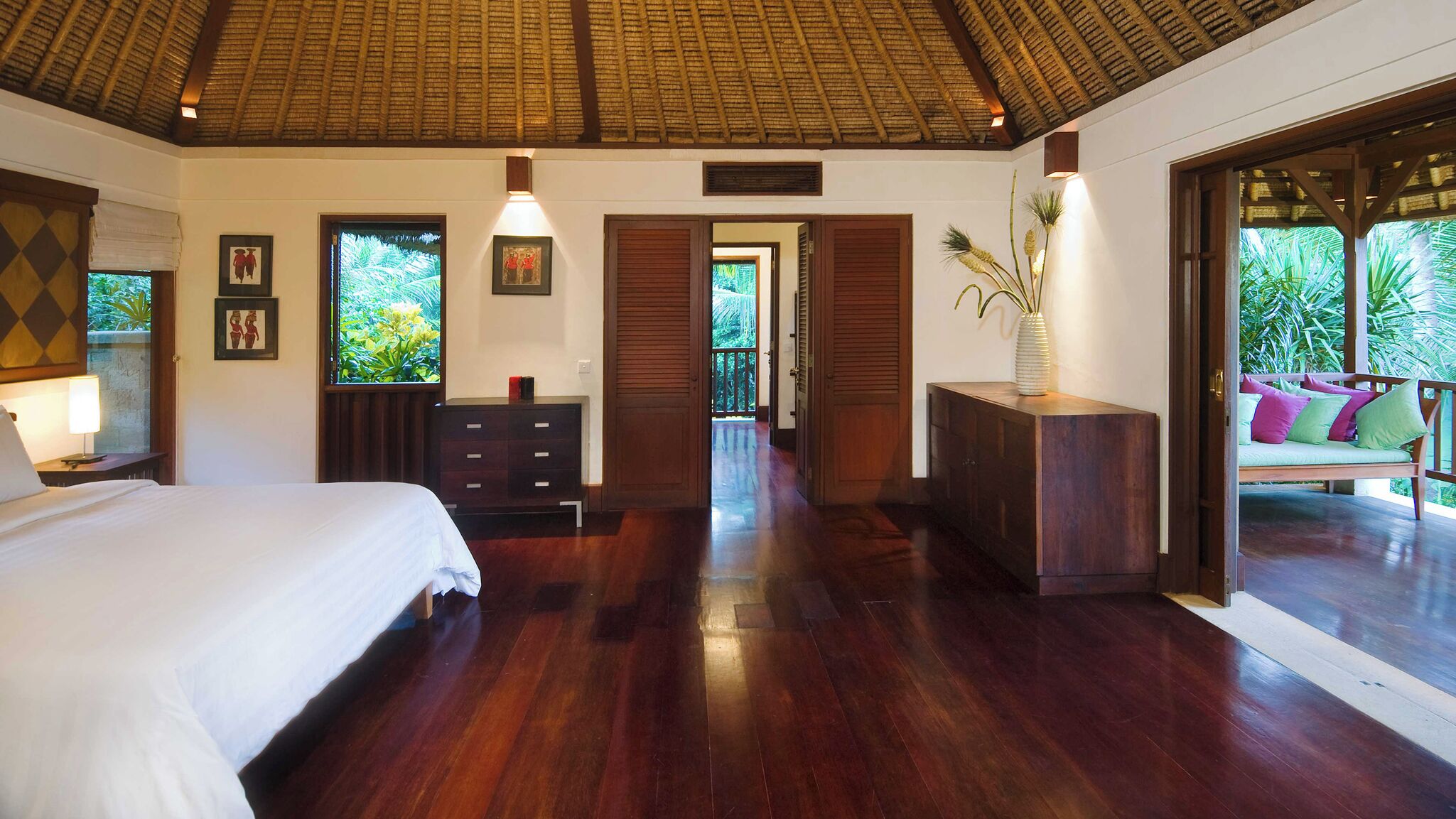 A spacious bedroom with a large bed, wooden furniture, and a view of lush greenery outside.