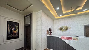 A reception area with a marble counter, a framed artwork of a deer, a statue, and a ceiling fan. - Hotel Vrinda orchid Inn (Vrindavan)