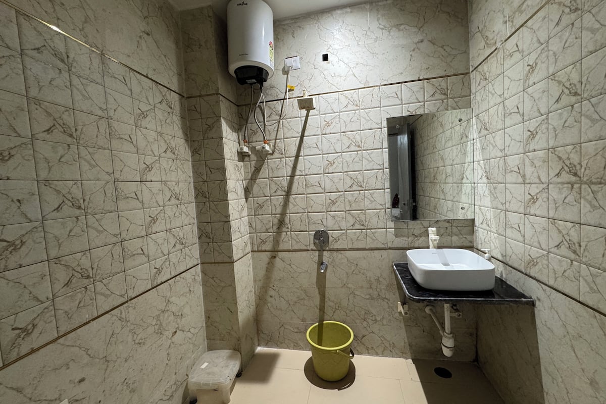 A bathroom with marble tiles, a white sink, a mirror, a yellow bucket, and a white heater.