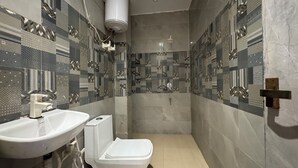 A modern bathroom with a sink, toilet, and shower. The walls are tiled with geometric patterns. - Hotel Vrinda orchid Inn (Vrindavan)