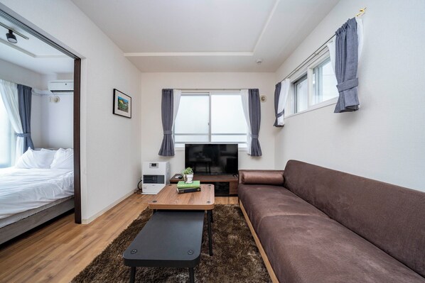 A modern, compact living space with a bed, sofa, TV, and a small table with a plant. - ANAX NORD 203 (Sapporo)