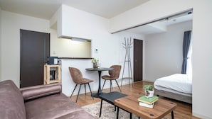 Ett modernt hotellrum med en soffa, ett litet matbord med stolar, en säng, ett skrivbord med en stol och ett stort fönster.