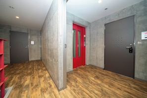 A hallway with wooden flooring, grey walls, and two doors, one red and one grey. - ANAX NORD 203 (Sapporo)