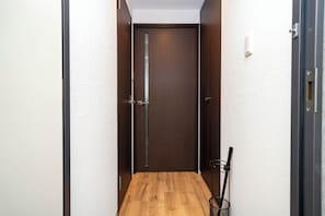 A narrow hallway with a wooden floor, a dark wooden door, and a metal rack with a broom. - ANAX NORD 203 (Sapporo)