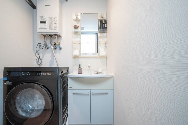 Une petite buanderie équipée d’un lave-linge à chargement frontal, d’un évier avec un miroir au-dessus et d’un petit meuble de rangement en dessous.