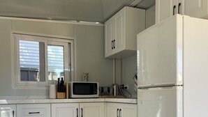 Eine moderne Küche mit weißen Schränken, einem weißen Kühlschrank, einer Mikrowelle und einem Fenster mit Jalousien.