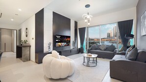 Een moderne woonkamer met een groot raam, een grijze bank, een witte poef en een televisie aan de muur.