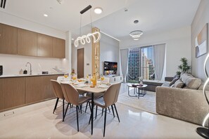 A modern living space with a dining area, kitchen, and a large window offering a city view. - Grande Suites by Hostiva - Burj View (Dubai)