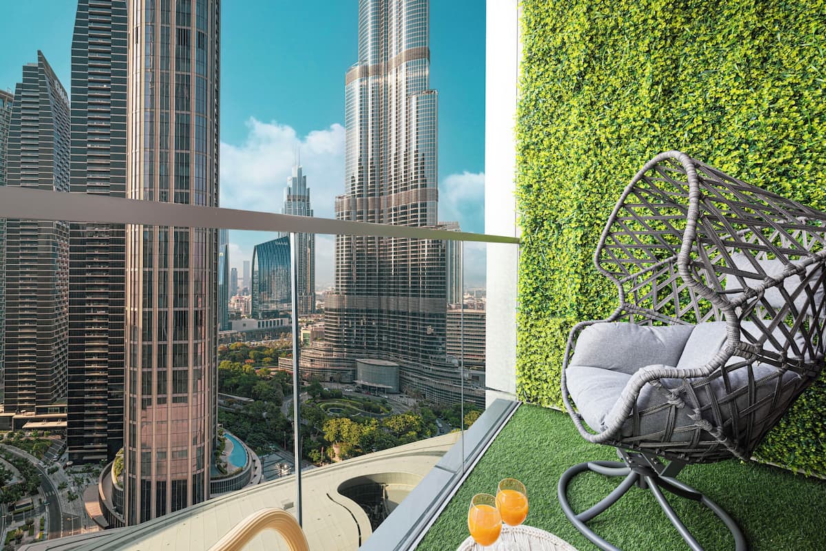 A balcony with a view of a cityscape, a wicker chair, and two glasses of orange juice on a table.