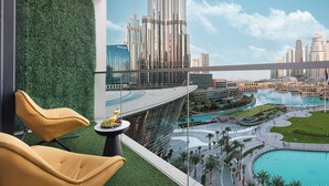 Een moderne hotelkamer met balkon met uitzicht op een stadsbeeld, een zwembad en een aangelegde tuin.