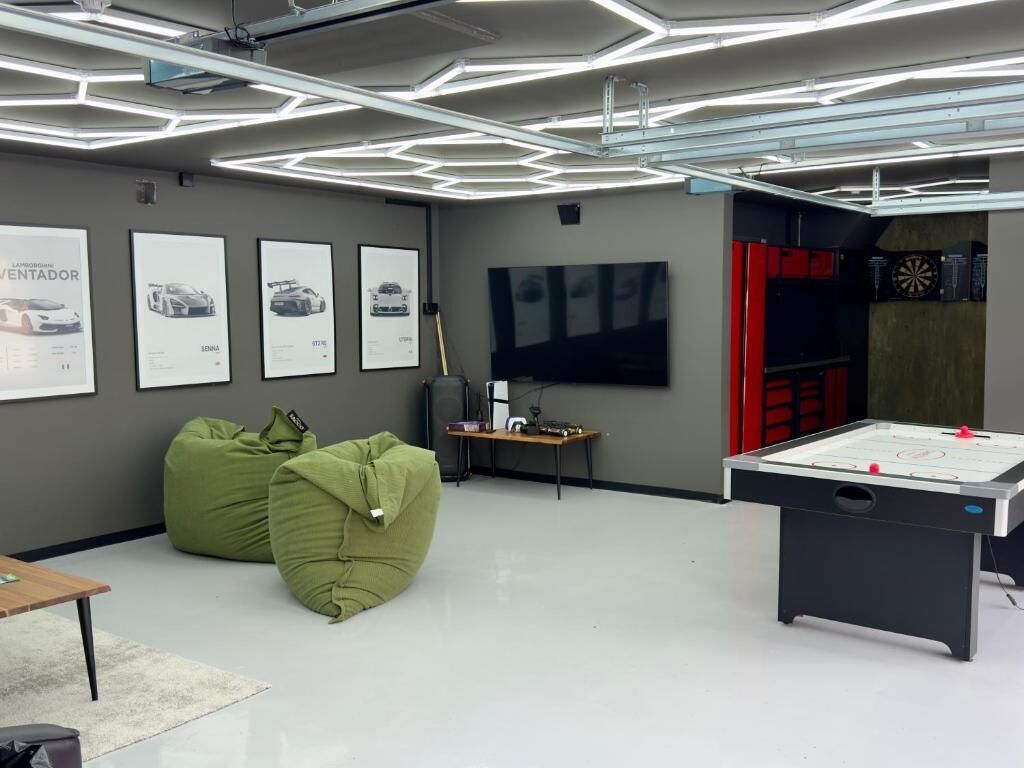 Una habitación moderna con luces de techo hexagonales, pufs verdes, un dardo y una mesa de futbolín.