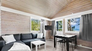 A modern living room with a grey sofa, white coffee table, and a dining area with a table and chairs. - Nordica Resort Florø (Kinn)