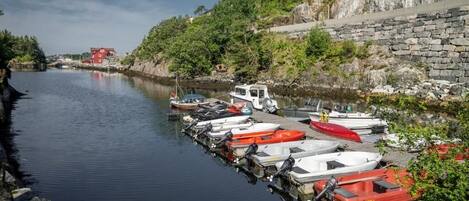 Un puerto deportivo con barcos amarrados a lo largo de un río tranquilo, rodeado de vegetación y un muro de piedra.