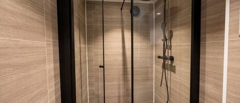A modern shower with a glass door, a handheld showerhead, and a wall-mounted control panel.