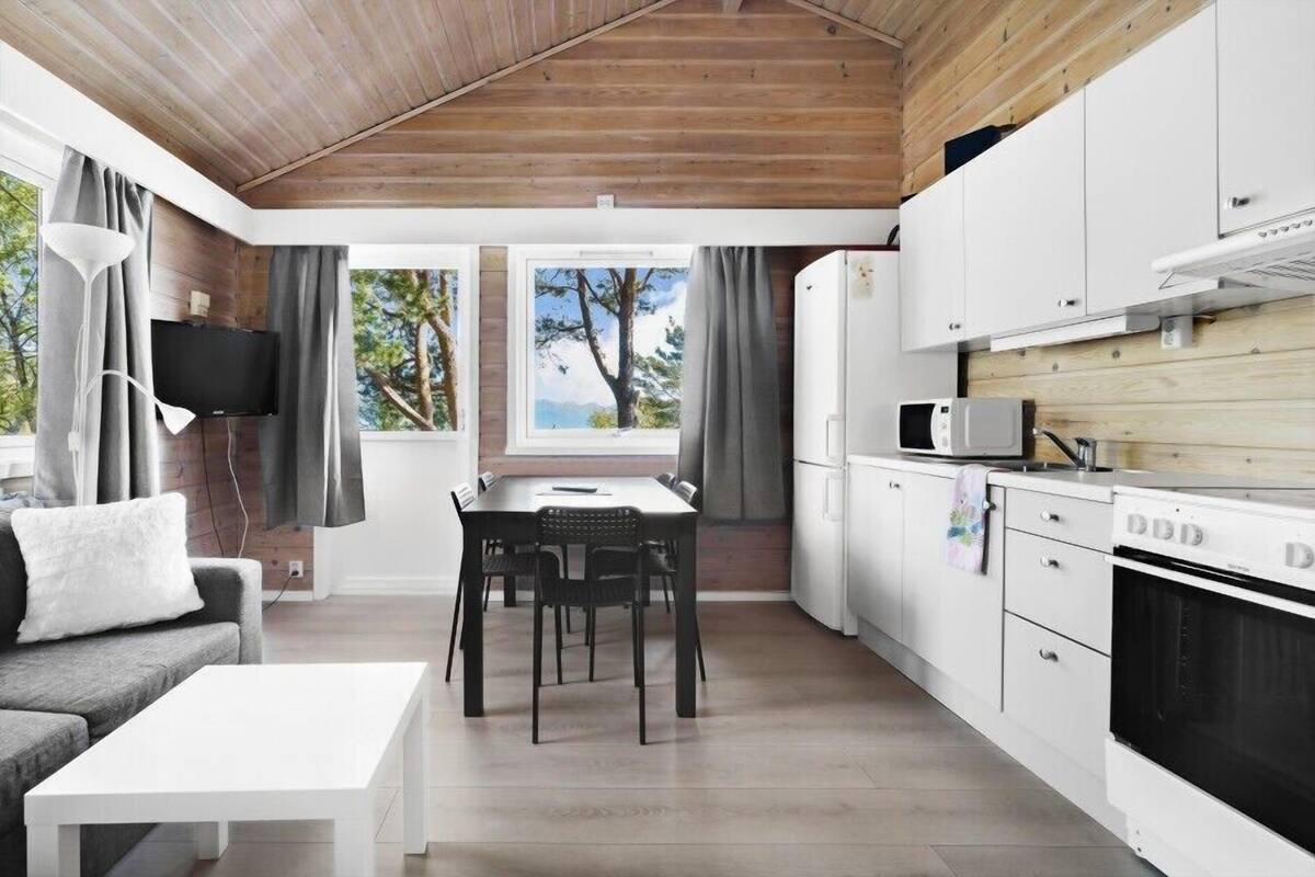 Una cocina moderna con armarios blancos, un microondas y una estufa. Hay una mesa de comedor con sillas y un sofá con un cojín blanco.