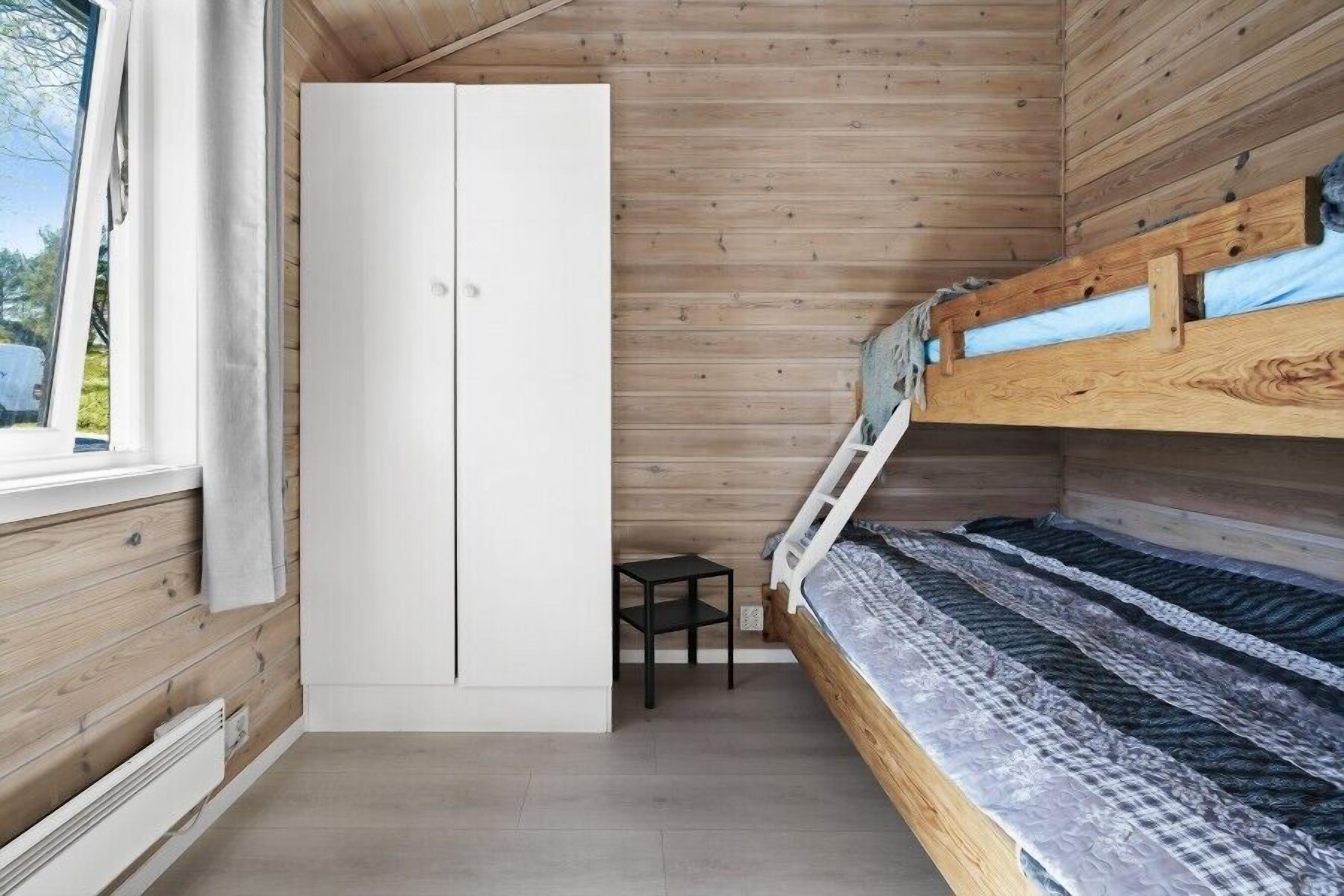A compact bedroom with a bunk bed, a wardrobe, and a small table.