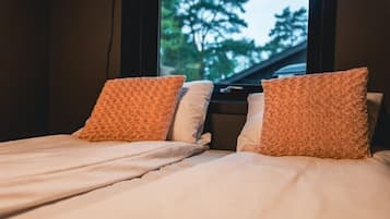 Cama con dos almohadas y una ventana con vista a árboles.