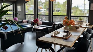 A modern lounge area with a pool table, chess set, and comfortable seating. Large windows offer views of the outdoors. - Nordica Resort Florø (Kinn)