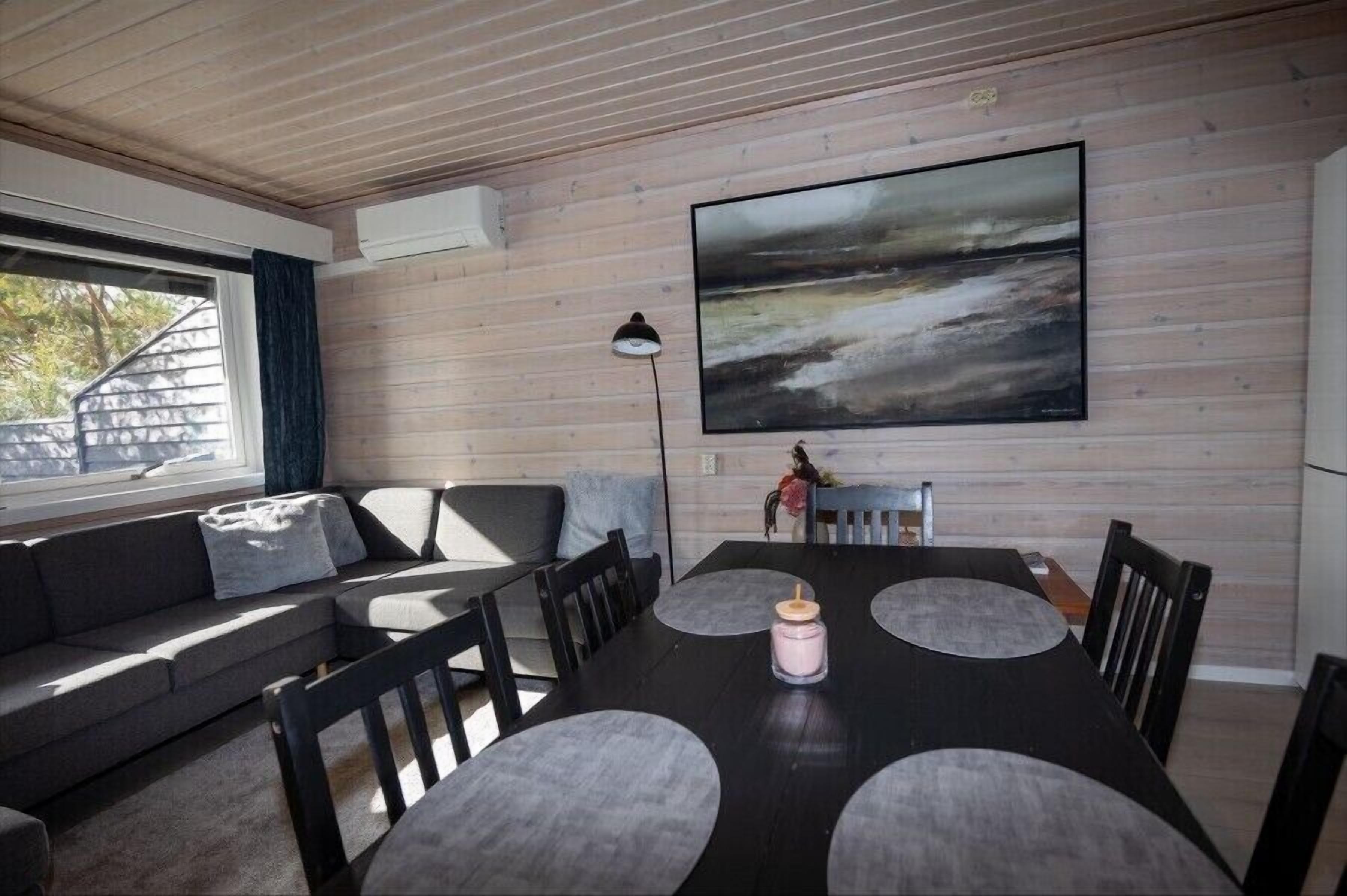A modern living room with a large painting, a sofa, and a dining table with chairs.