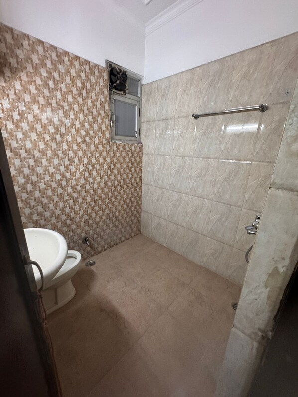 A bathroom with a toilet, a shower, and a tiled wall.