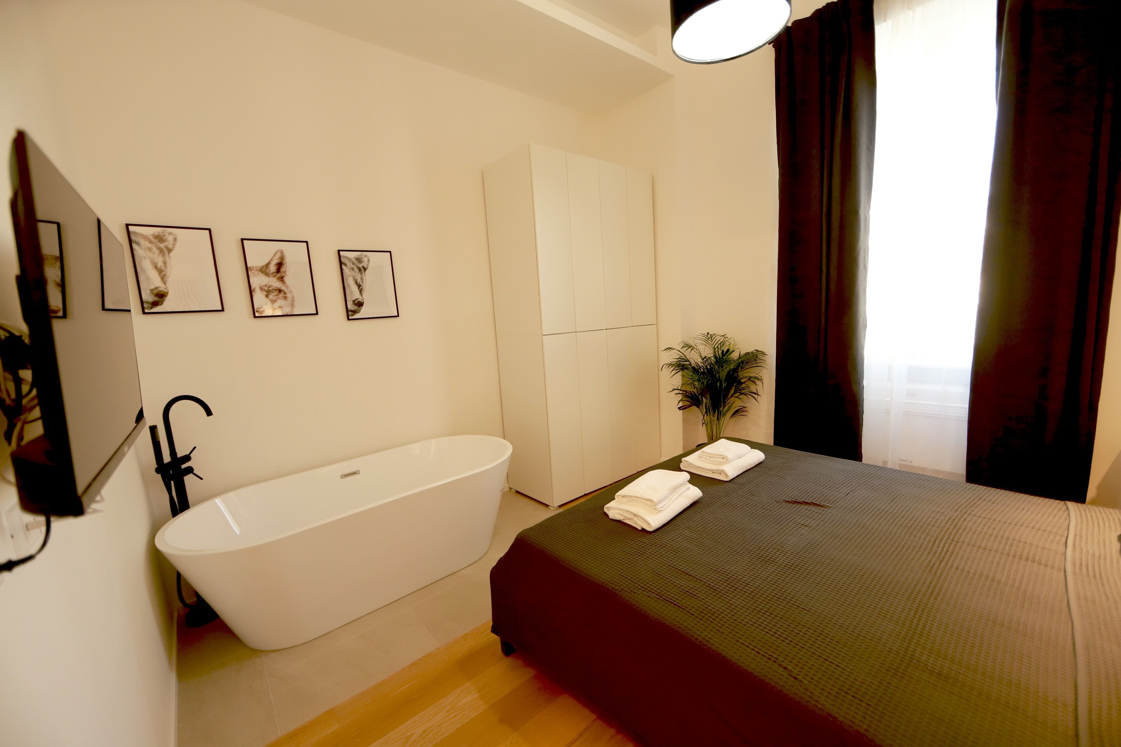 A modern bathroom with a freestanding bathtub, a bed with a green bedspread, and a wall-mounted sink.
