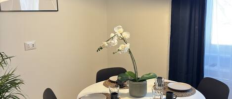 A modern dining area with a round table, black chairs, woven placemats, and a potted orchid.