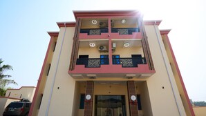 Un edificio de varios pisos con una entrada central, balcones en cada planta y un coche estacionado adelante.