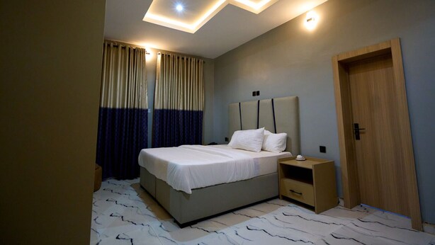 Un dormitorio moderno con una cama, mesitas de noche, una puerta de madera e iluminación empotrada en el techo.
