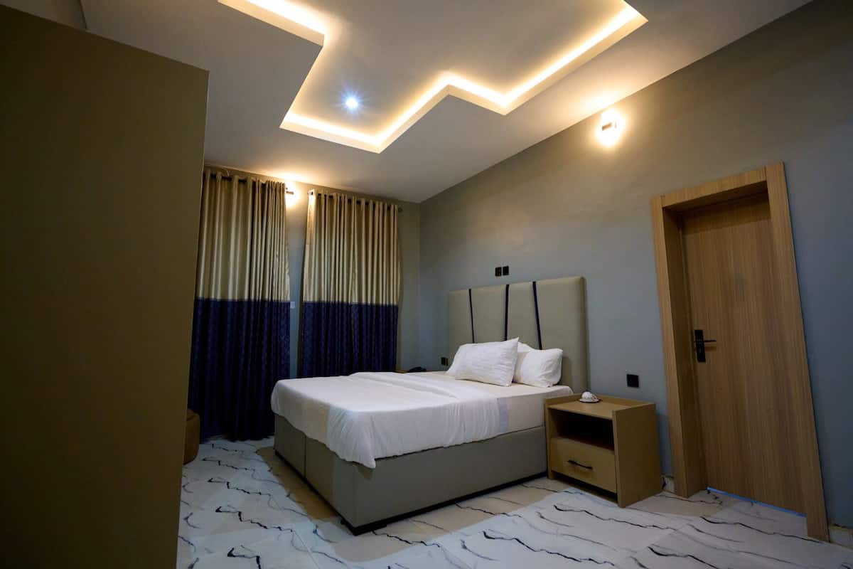 A modern bedroom with a bed, nightstands, a wooden door, and a ceiling with recessed lighting.