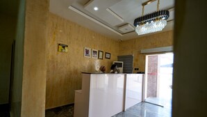 Un área de recepción con suelo de mármol, mostrador de recepción, candelabro y certificados enmarcados en la pared.