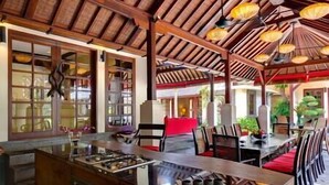Un restaurante con techo de madera, una isla central con una parrilla y sillas rojas.