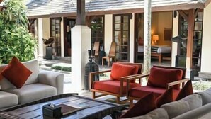 Un área de estar moderna al aire libre con sofá y sillones, una mesa de centro y vistas del interior del edificio.