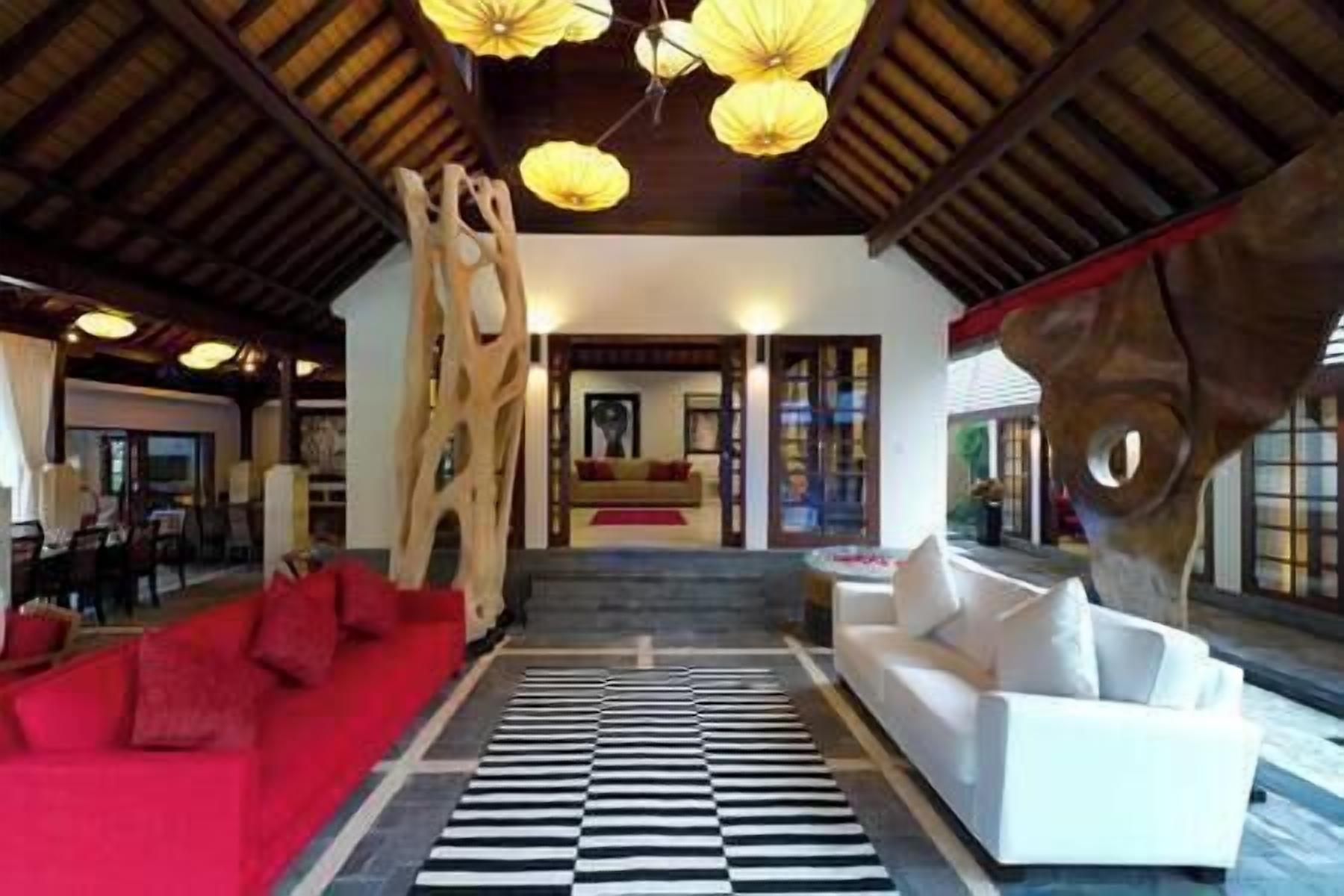 A spacious lobby with a red sofa, a white sofa, and a black and white striped rug. There are hanging lights and a large wooden sculpture.