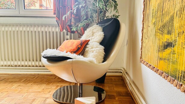 A modern room with a leather armchair, a small ottoman, a potted plant, and a window with a view of buildings. - Room 'Sternenzimmer' with Wi-Fi (KASSEL)