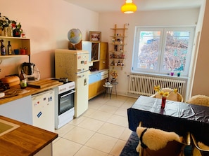 A compact kitchen with a stove, oven, refrigerator, and a dining table with chairs.
